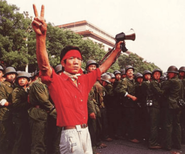Le 3 juin, un manifestant étudiant pro-démocratie montre des signes de victoire à la foule, alors que les troupes se retirent du côté ouest du Grand Hall du Peuple près de la place Tiananmen. (Image : Domaine public)