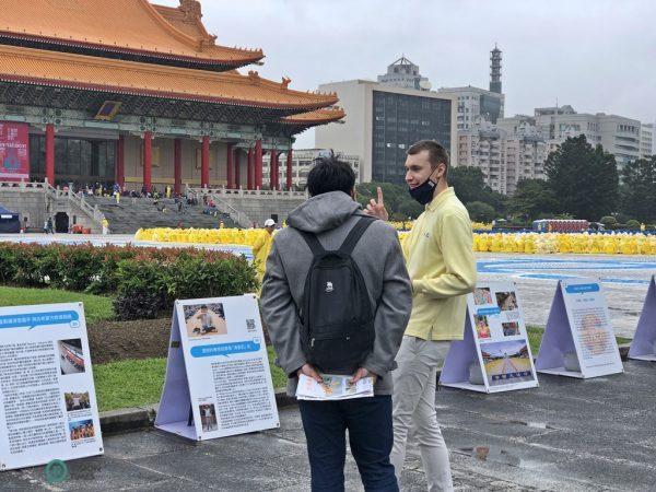 Un pratiquant de Falun Gong d’Europe explique la magnificence de la formation des caractères, devant des panneaux d’affichage présentant le Falun Gong sur la Place de la Liberté.  (Image: Billy Shyu / Vision Times)